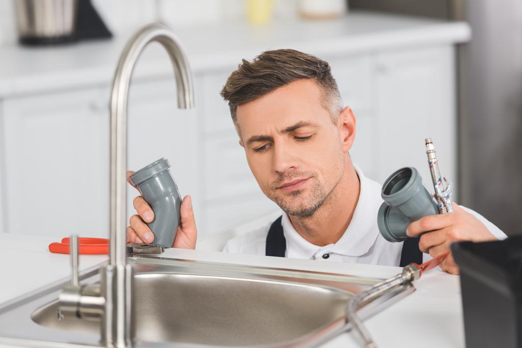 pozorné dospělé opravář držení nástroje a potrubí při opravě kohoutek v kuchyni  - Fotografie, Obrázek