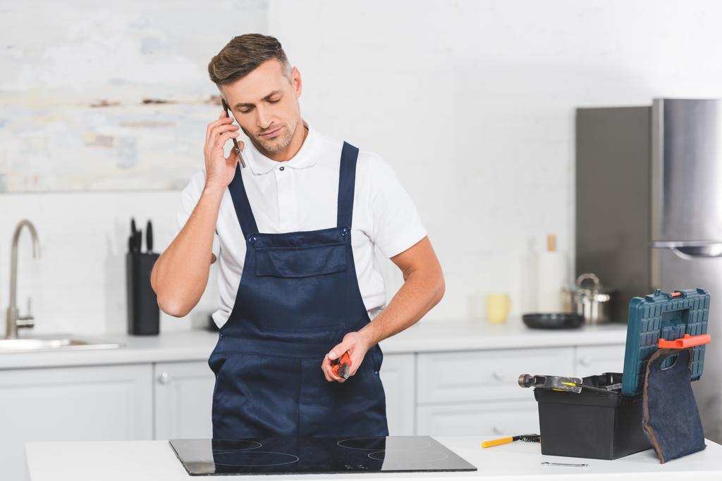 réparateur adulte parlant sur smartphone et tenant pinces tout en réparant cuisinière électrique
 - Photo, image