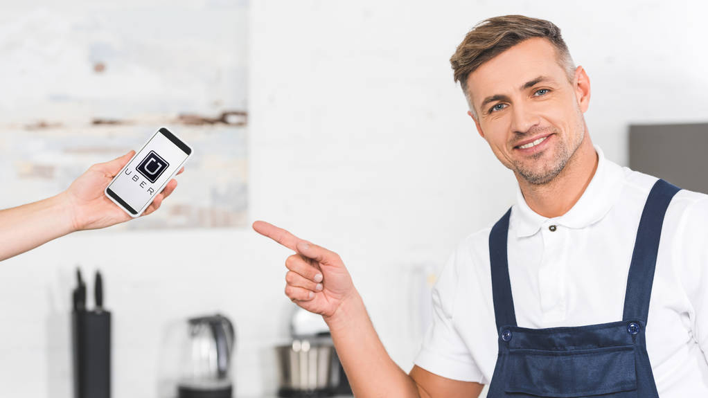 partial view of hand holding smartphone and smiling adult repairman pointing with finger at screen with uber app  - Photo, Image