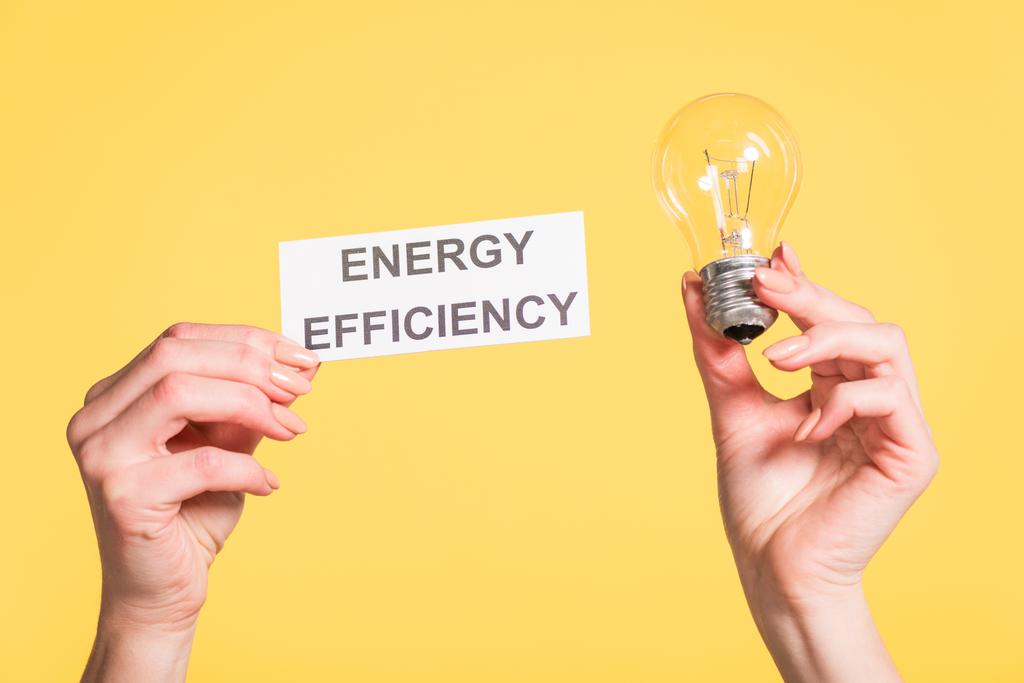 visão recortada de mãos femininas segurando lâmpada led e cartão de papel com letras isoladas em amarelo, conceito de eficiência energética
 - Foto, Imagem
