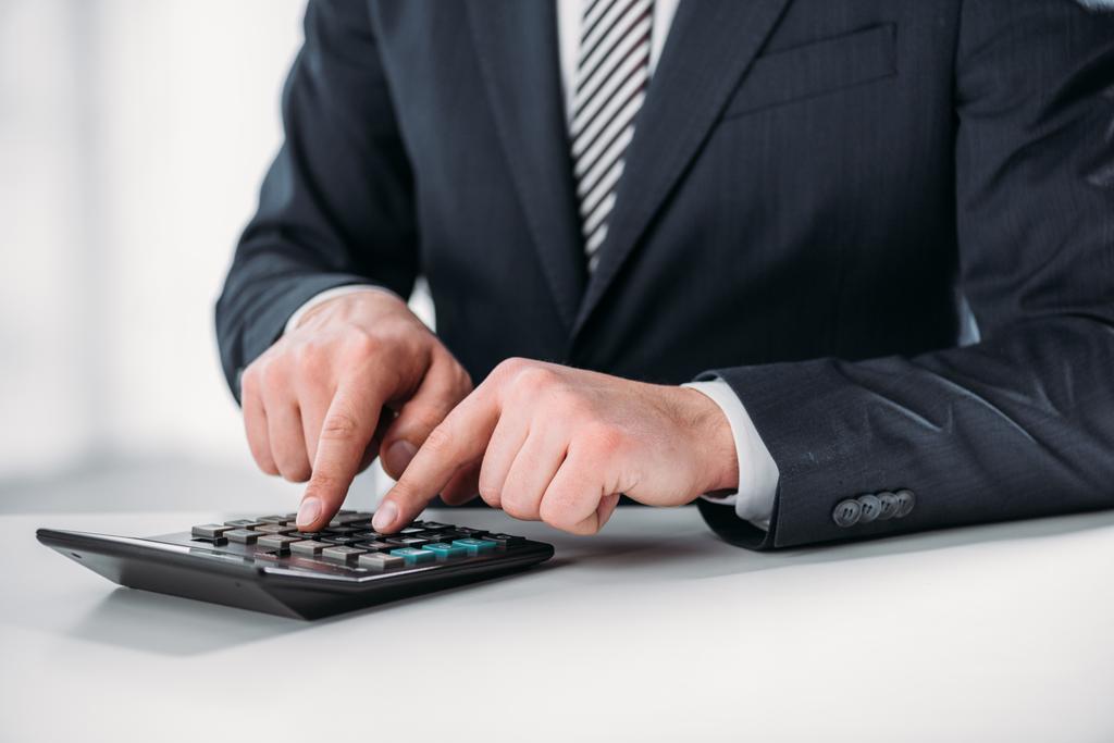 vista cortada do homem de negócios em terno usando calculadora em fundo branco, conceito de eficiência energética
 - Foto, Imagem