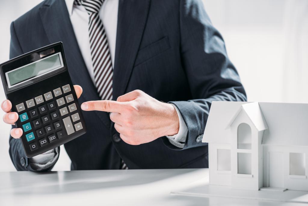 cropped view of businessman pointing with finger at calculator near carton house on white background , energy efficiency concept - Photo, Image
