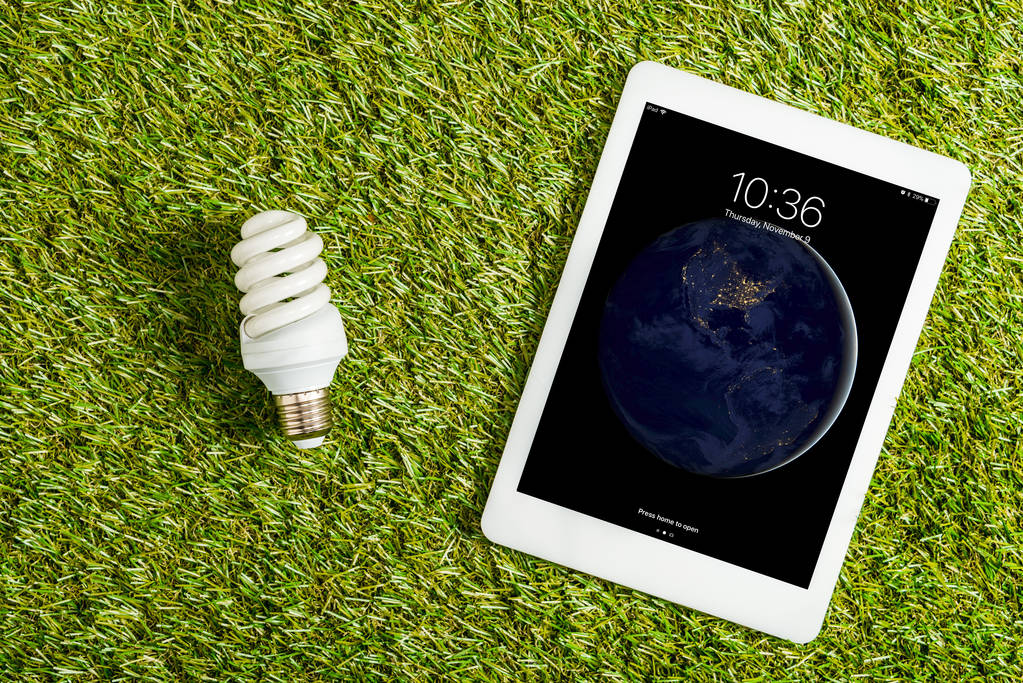 Widok z góry świetlówki w pobliżu cyfrowy tablet z ekranem blokady na zielonej trawie, pojęcie efektywności energetycznej - Zdjęcie, obraz