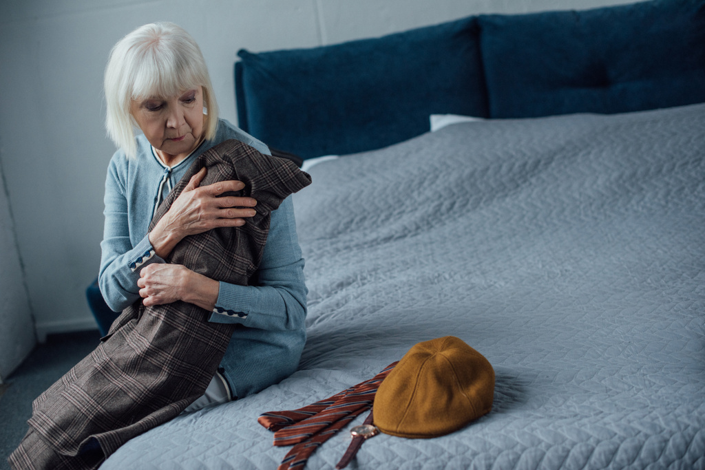 boos senior vrouw zittend op bed en jas thuis houden - Foto, afbeelding