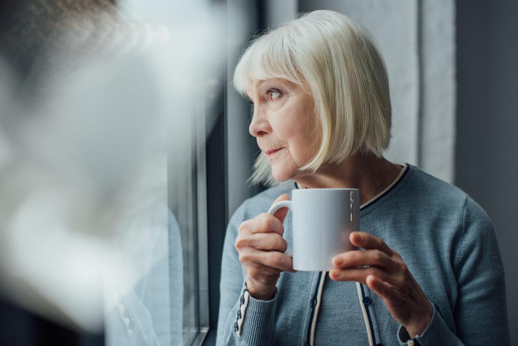 gondolkodó idősebb nő otthon tartja a kávét, és keres el - Fotó, kép