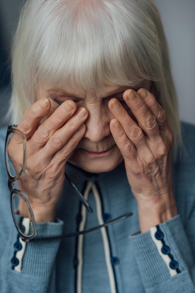 Portret van senior vrouw met glazen en grijs haar veegde tranen en huilen thuis - Foto, afbeelding