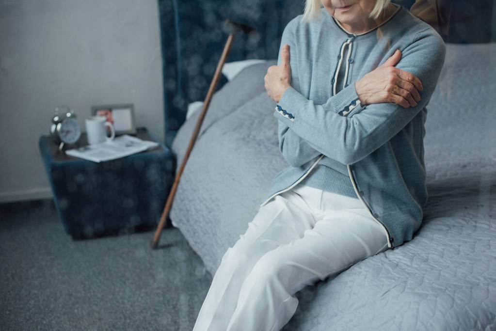 vue recadrée de femme âgée solitaire assise sur le lit avec les mains croisées à la maison
 - Photo, image