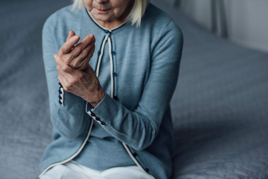 partial view of senior woman sitting on bed and measuring pulse with hand at home - Photo, Image