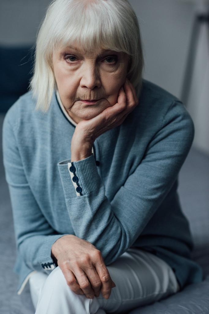 mujer mayor disgustada con el pelo gris apoyando la barbilla con la mano y mirando a la cámara en casa
 - Foto, Imagen