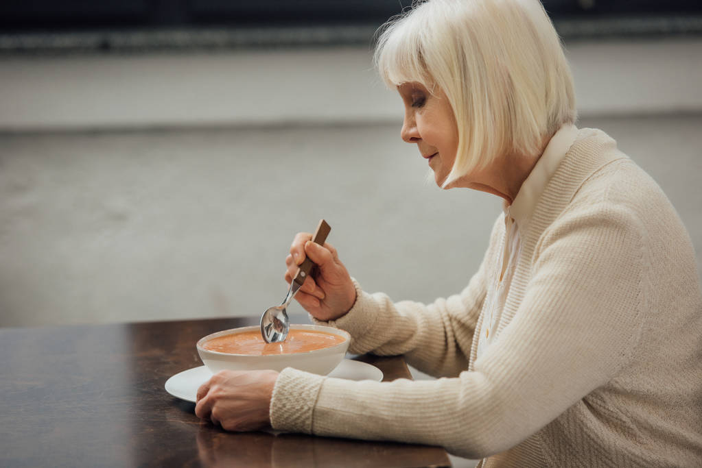 triste anciana sentada en la mesa y comiendo sopa de crema en casa
 - Foto, Imagen
