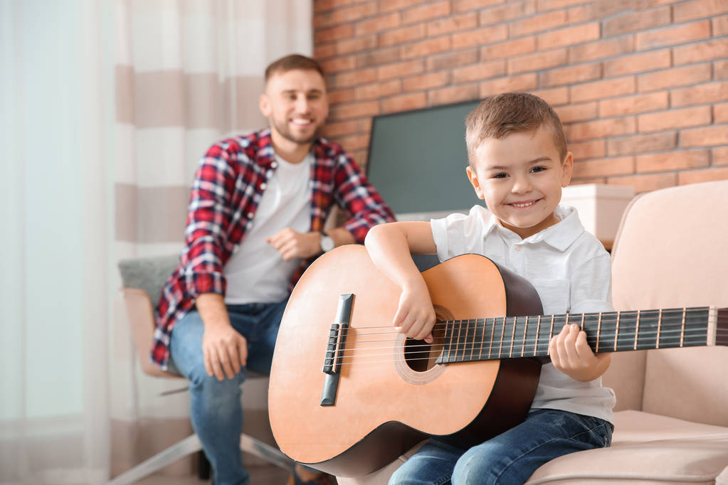 Батько дивиться, як його син грає на гітарі вдома
 - Фото, зображення