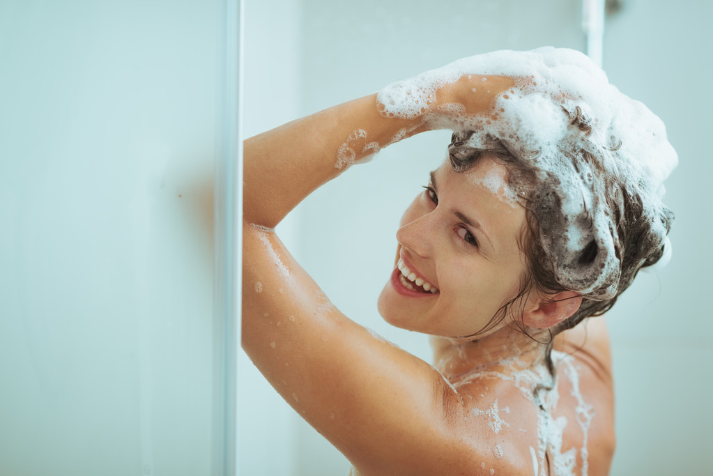 Улыбающаяся молодая женщина моет голову шампунем
 - Фото, изображение