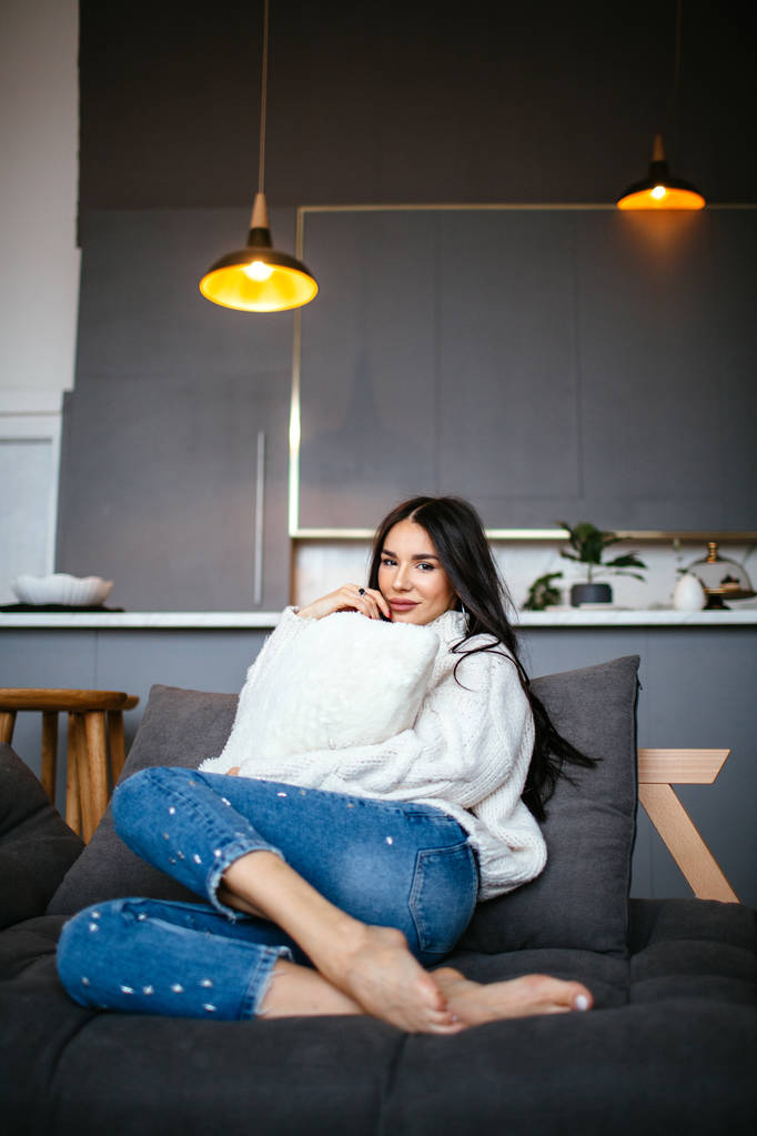 Красивая девушка в белой куртке и джинсах отдыхает дома на диване. портрет, скандинавский стиль
 - Фото, изображение