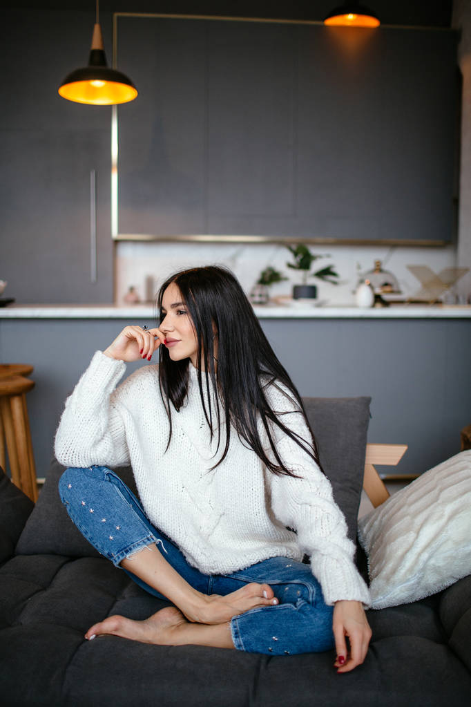 Bella ragazza in giacca bianca e jeans si riposa sul divano di casa. ritratto, stile scandinavo
 - Foto, immagini