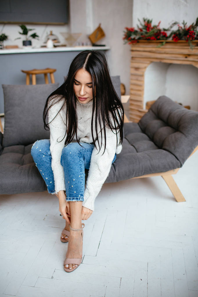 Belle fille dans une veste blanche et un jean se repose sur le canapé à la maison. portrait, style scandinave
 - Photo, image
