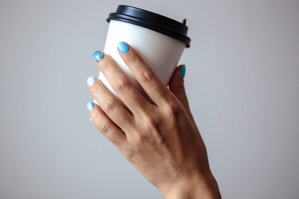 Gorgeous manicure, pastel tender blue color nail polish, closeup photo. Female hands hold a plastic coffee cup over simple background  - Photo, Image
