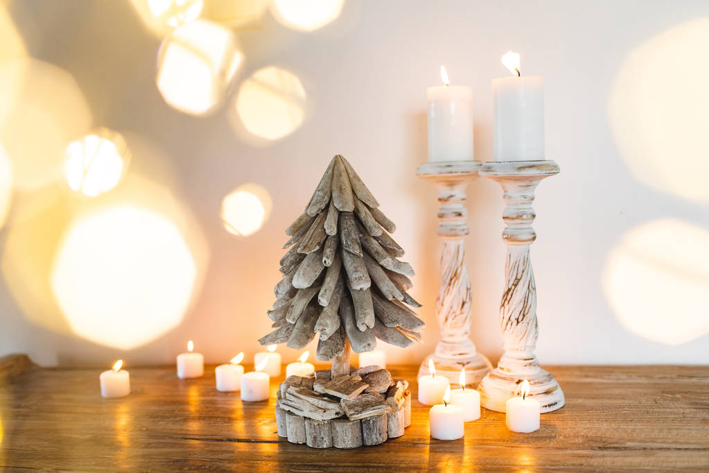Белая деревянная украшенная елка со свечами и золотыми размытыми сияющими огнями вокруг. Место для смс. Праздничная концепция ручной работы
 - Фото, изображение