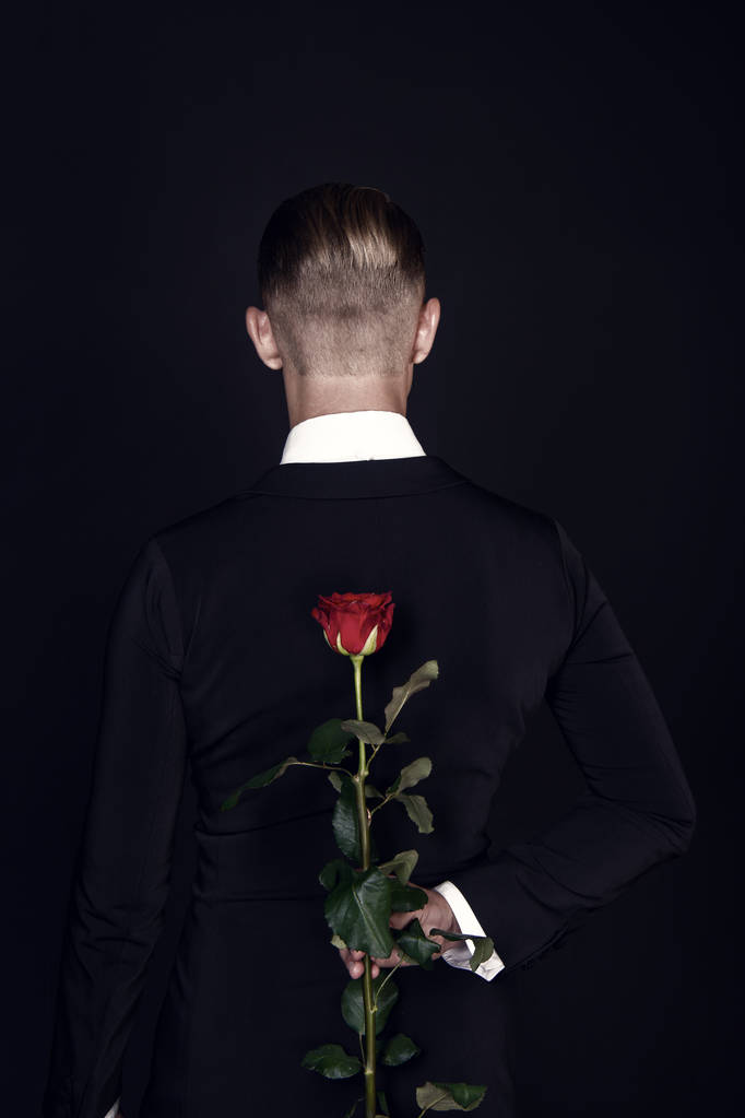 Чоловік ховає червону троянду позаду, вид ззаду
 - Фото, зображення