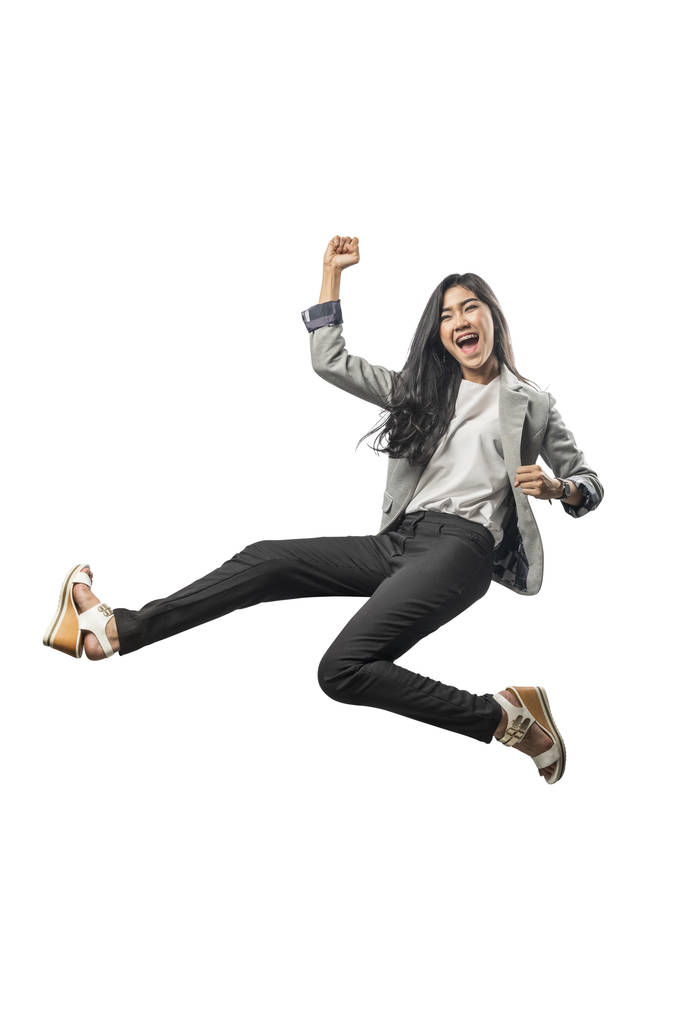erfolgreiche asiatische Geschäftsfrau springt und hebt den Arm in die Luft, posiert isoliert vor weißem Hintergrund - Foto, Bild