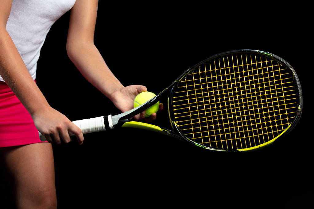 Νεαρή γυναίκα σε μια πρακτική τένις. Αρχάριος παίκτης που κρατάει μια ρακέτα, εκμάθηση βασικών δεξιοτήτων. Πορτραίτο σε μαύρο φόντο. - Φωτογραφία, εικόνα