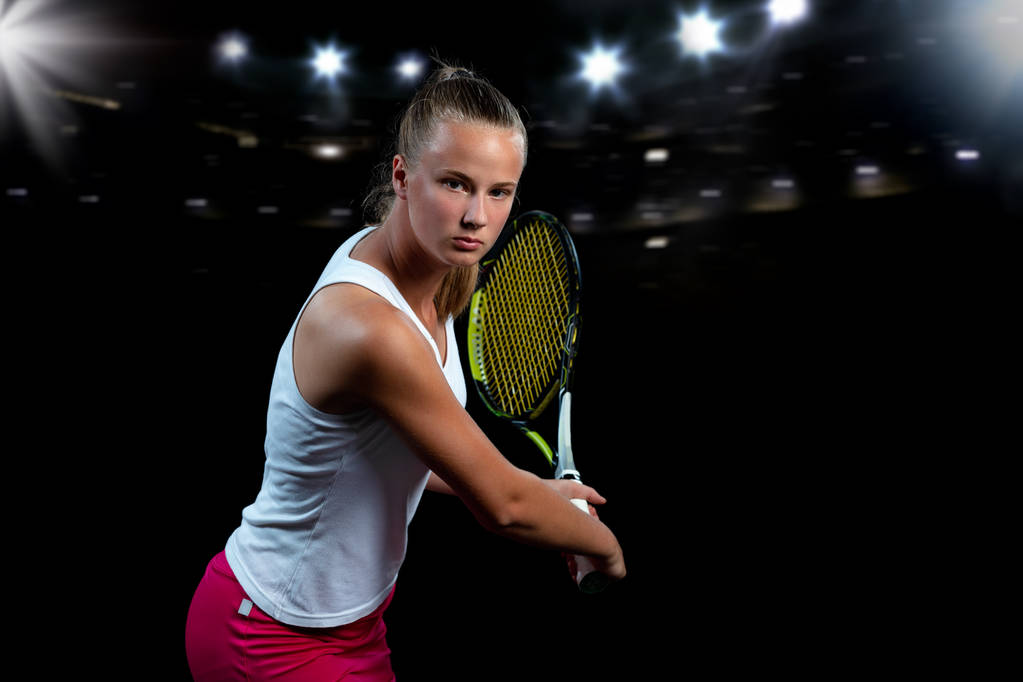 Mooi meisje tennisspeler met een racket op donkere achtergrond met verlichting - Foto, afbeelding