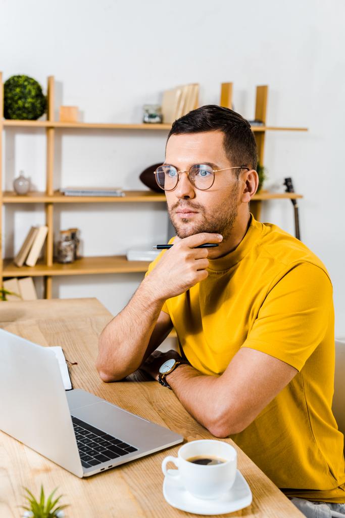 přemýšlivý muž sedící v brýlích poblíž laptop a šálek kávy - Fotografie, Obrázek