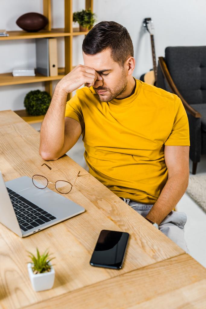 väsynyt mies istuu läppärin ja älypuhelimen lähellä kotona
 - Valokuva, kuva