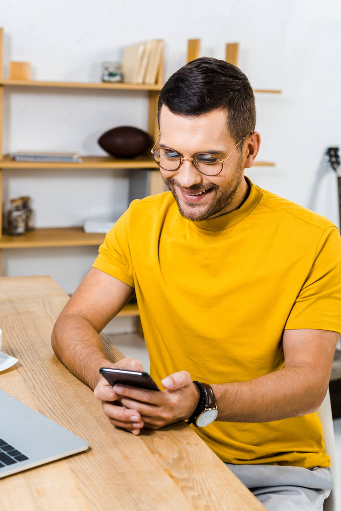 όμορφος άντρας χαμογελώντας ενώ βλέπουν το smartphone στο σπίτι - Φωτογραφία, εικόνα