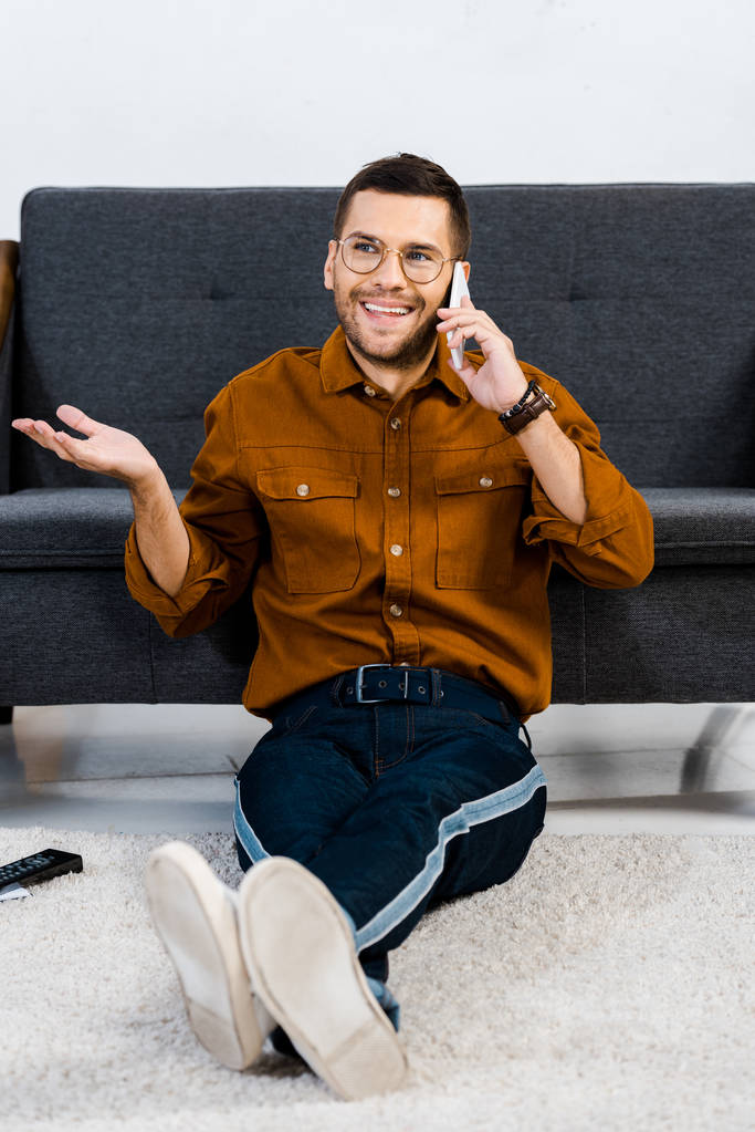 wesoły człowiek siedzi na dywanie i mówić na smartphone  - Zdjęcie, obraz