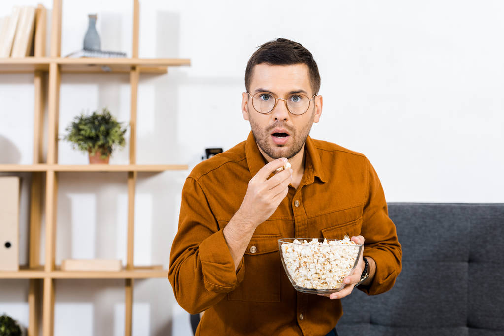 překvapený muž v brýlích jíst popcorn v obývacím pokoji - Fotografie, Obrázek