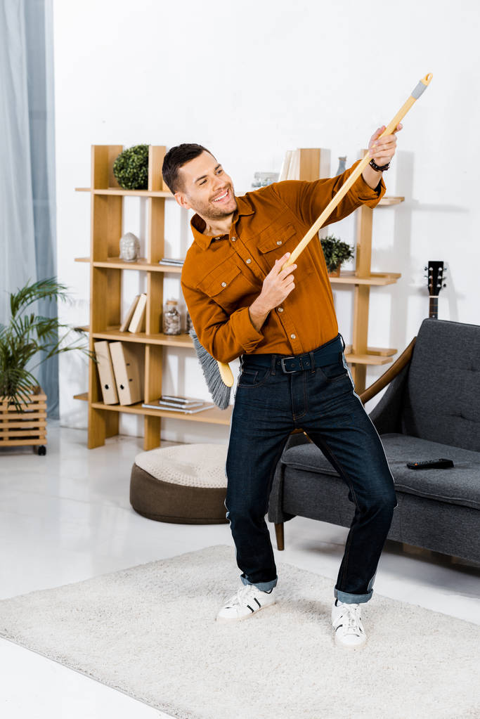 homem bonito dançando com vassoura na sala de estar moderna
  - Foto, Imagem