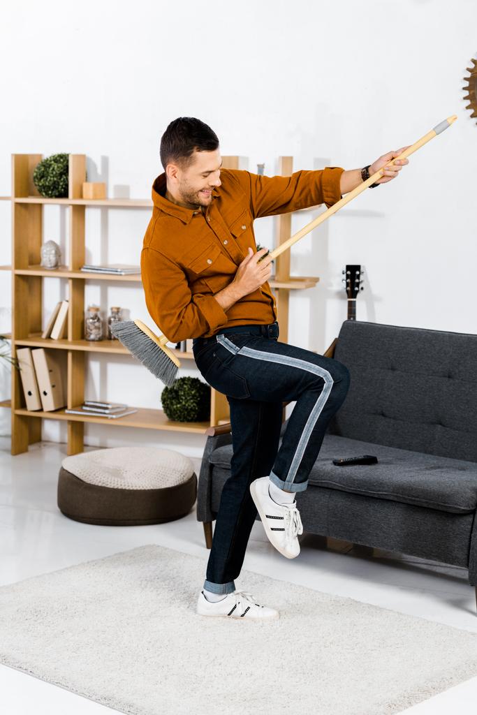 homem alegre dançando com vassoura na sala de estar moderna
  - Foto, Imagem