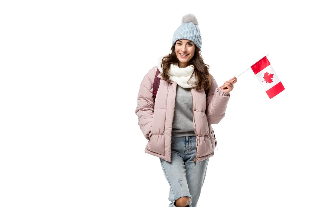 usměvavá studentka v zimní oblečení drží kanadské vlajky a při pohledu na fotoaparát izolované na bílém - Fotografie, Obrázek