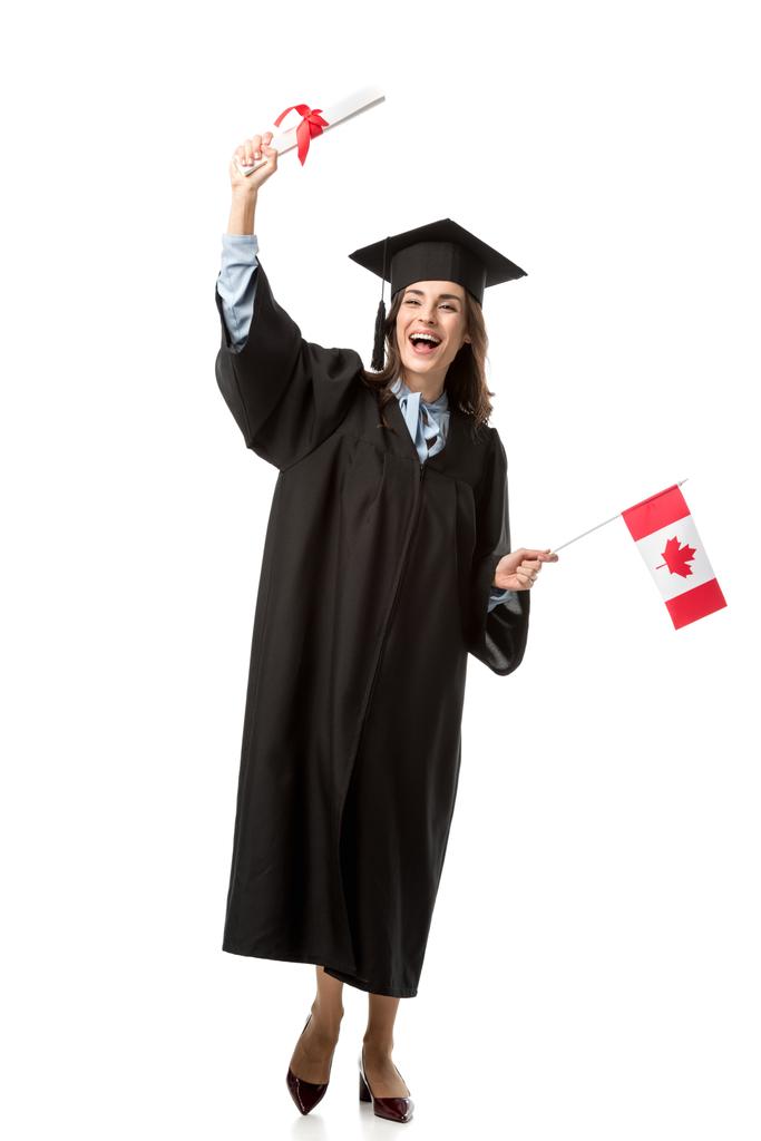 ευτυχισμένος φοιτήτριας σε ακαδημαϊκό φόρεμα εκμετάλλευση καναδική σημαία και δίπλωμα που απομονώνονται σε λευκό - Φωτογραφία, εικόνα