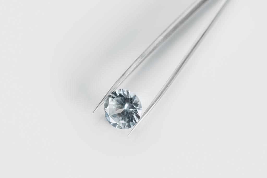 bovenaanzicht van glanzende diamant in pincet op witte achtergrond - Foto, afbeelding