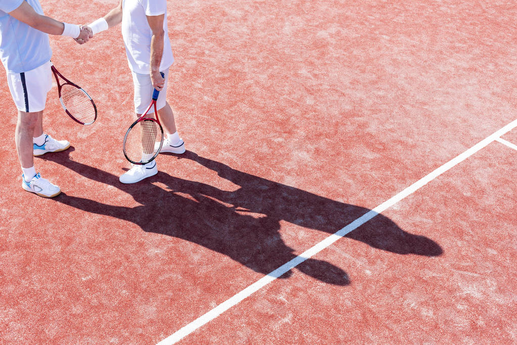 Low section of mature men shaking hands while standing on tennis court during match - Photo, Image