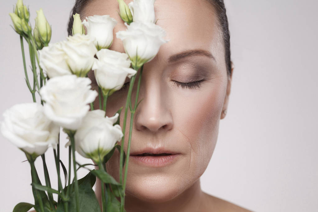 retrato de mujer madura con piel perfecta y arrugas envejecidas apoyadas en flores
 - Foto, Imagen