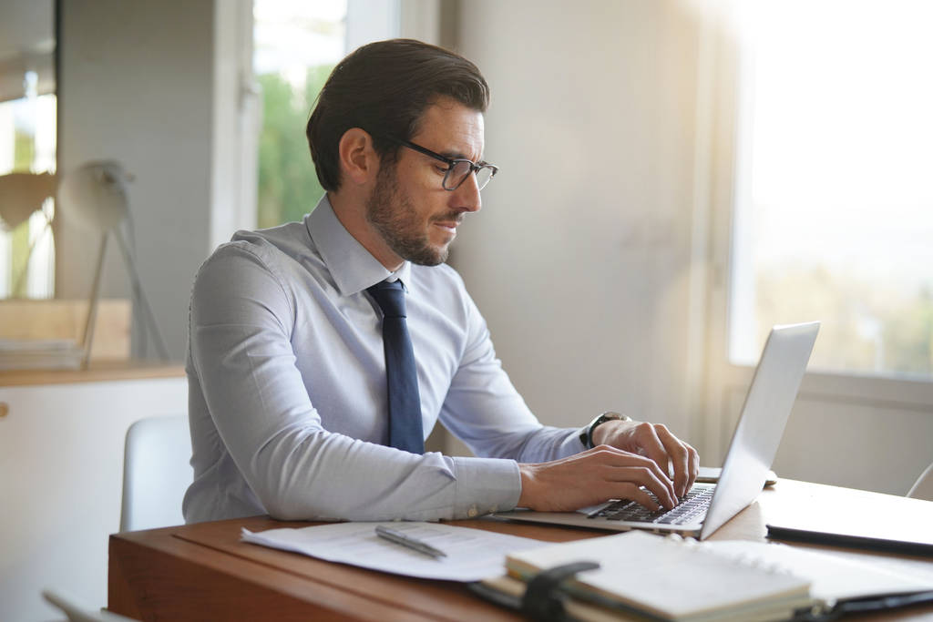 Empresário atraente digitando no laptop no escritório moderno
 - Foto, Imagem