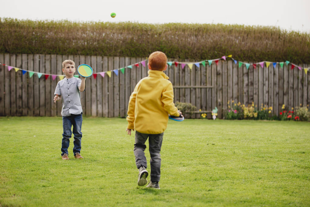 Dos jóvenes jugando afuera en un jardín trasero. Se lanzan una pelota de tenis y la atrapan con un guante de velcro.
. - Foto, imagen