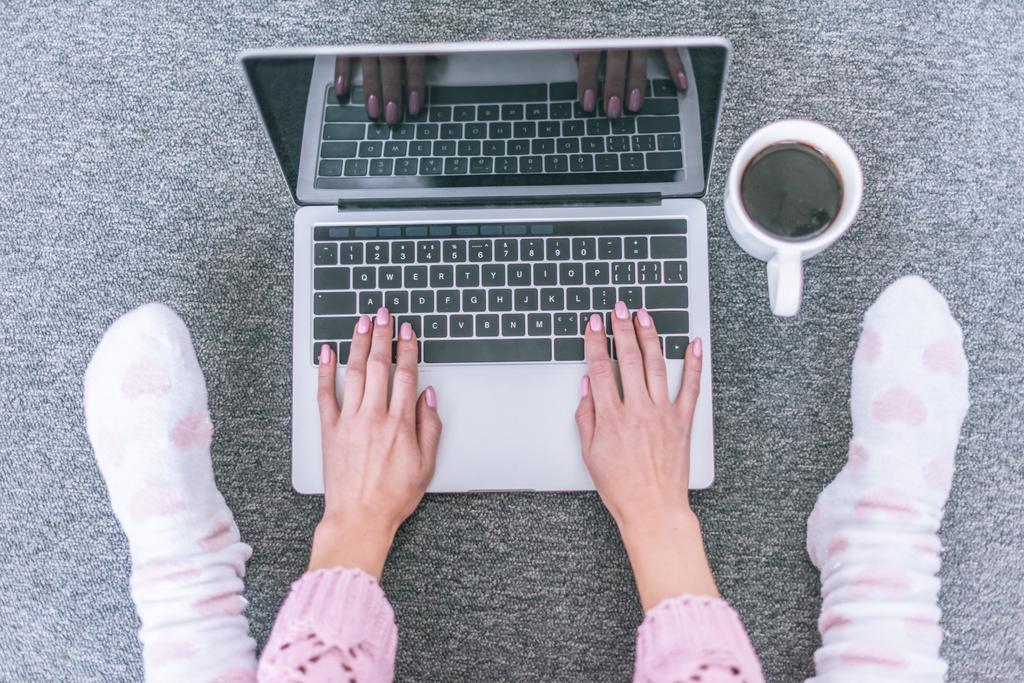 bovenaanzicht van vrouwelijke blogger te typen op het toetsenbord van de laptop in de buurt van kopje koffie - Foto, afbeelding