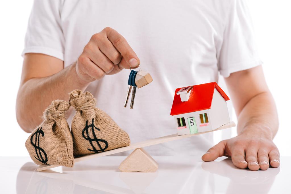 partial view of man holding keys near moneybags and house model on scales isolated on white, mortgage concept - Photo, Image