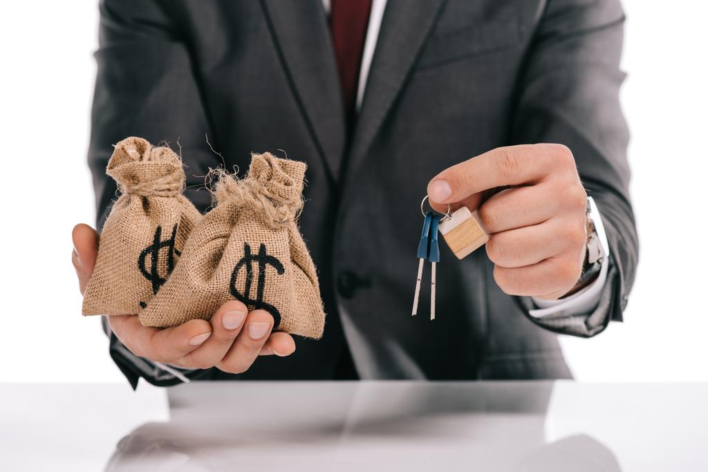 cropped view of mortgage broker holding keys and moneybags isolated on white - Photo, Image