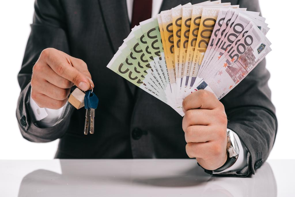 обрізаний вид бізнесмена, який тримає ключі і євро банкноти ізольовані на білому, іпотечна концепція
 - Фото, зображення