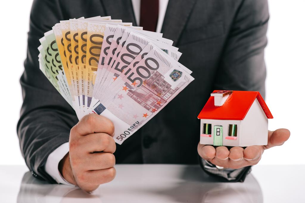 обрізаний вид бізнесмена, що тримає модель будинку та банкноти євро ізольовані на білому, іпотечна концепція
 - Фото, зображення