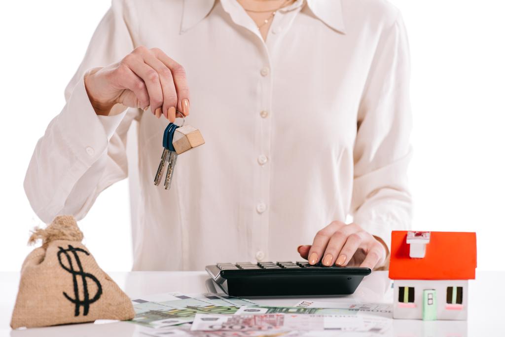 abgeschnittene Ansicht einer Geschäftsfrau, die Schlüssel hält und Taschenrechner benutzt, isoliert auf weißem, Hypothekenkonzept - Foto, Bild