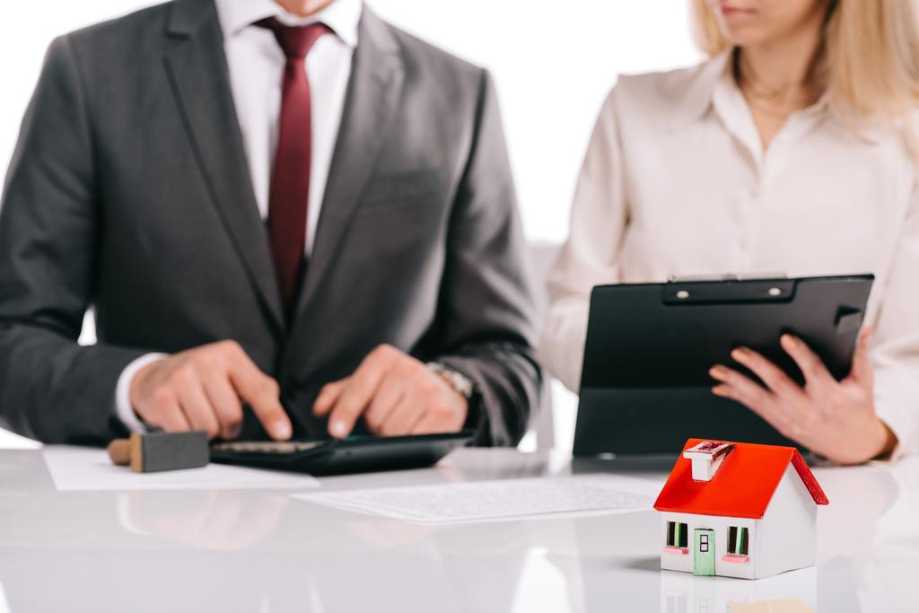 selektiver Fokus des Hausmodells mit Geschäftsleuten mit Taschenrechner und Klemmbrett isoliert auf weißem Hypothekenkonzept - Foto, Bild