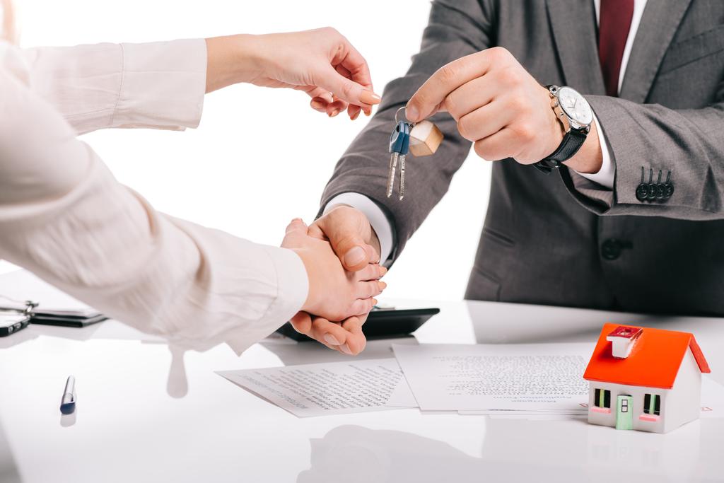 abgeschnittene Ansicht eines Hypothekenmaklers, der Frau die Hand schüttelt und Schlüssel isoliert auf weißem Grund hält, Hypothekenkonzept - Foto, Bild