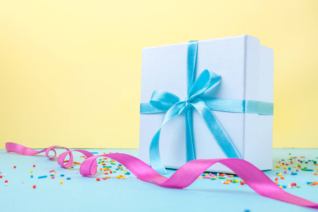 Cadeau, petite boîte attachée avec un ruban bleu satiné sur fond jaune. Concept cadeau. Félicitations pour les vacances, donnez des cadeaux. Espace de copie
  - Photo, image