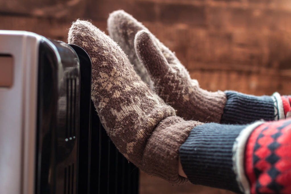 Women's hands in Christmas, warm, winter mittens on the heater. Keep warm in the winter, cold evenings. Heating seaso - Photo, Image