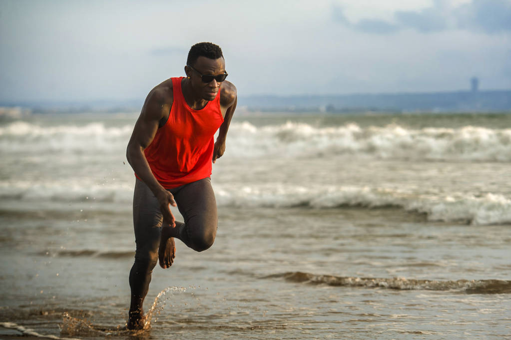 jovem atraente ajuste atlético e forte negro afro americano homem correndo na praia treinamento duro e sprint na água do mar no estilo de vida atleta profissional e rasgado corredor treino
  - Foto, Imagem